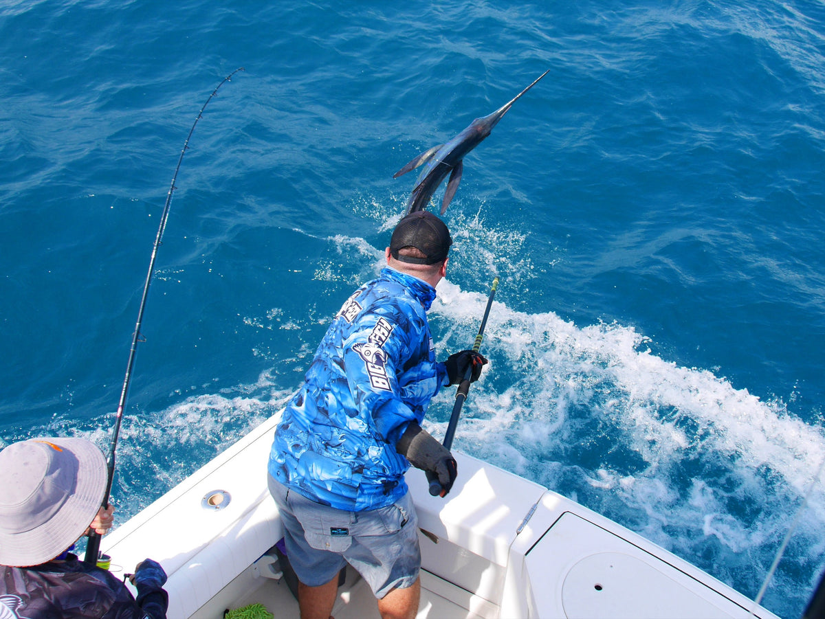 Angler in a Bigfish shirt leadering a jumping sailfish off the back of a boat